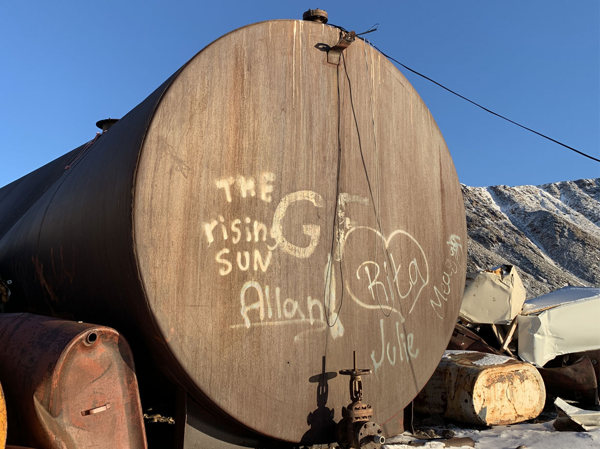 Blue clear sky with a Large diesel oil tank and two smaller oil tanks on snow covered ground.