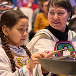 Une jeune Inuk allume la lampe Qulliq avec une Aînée.