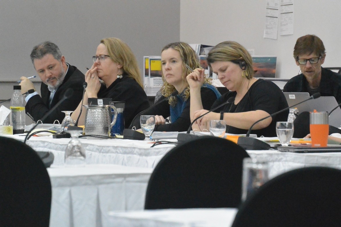 On voit 5&nbsp;personnes assises aux tables qui écoutent une présentation.
